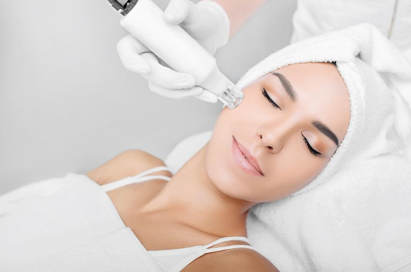 Une femme subit un traitement de la peau a l'aide d'un appareil de microneedling, tout en etant allongee et detendue avec une serviette autour de la tete.
