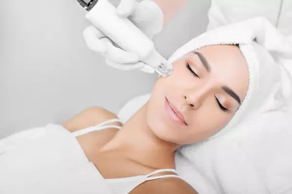 Une femme subit un traitement de la peau a l'aide d'un appareil de microneedling, tout en etant allongee et detendue avec une serviette autour de la tete.