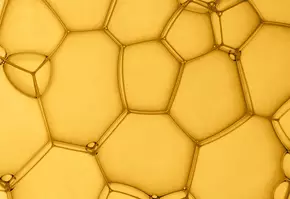 Detailopname van gouden zeepbellen met een honingraatstructuur, die een wervelende, speelse uitstraling heeft.