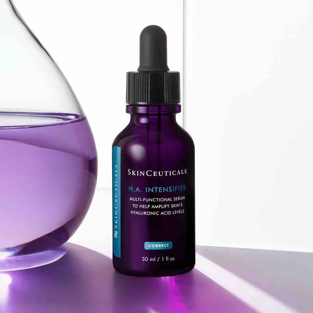 Een paarse fles huidserum van SkinCeuticals met een pipet, op een lichte achtergrond naast een glazen watercontainer.