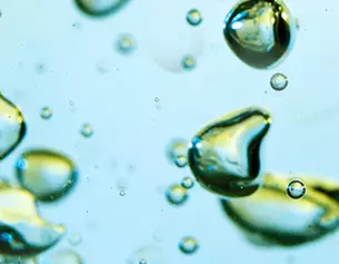 Gouttes de liquide de differentes tailles flottant dans un fond bleu, creant un effet de luminosite et de texture.