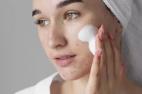 Une femme en serviette de bain appliquant un nettoyant moussant sur son visage, avec un aspect naturel et frais.