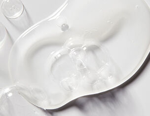 Clear, gel-like substance pooled on a smooth surface, reflecting light and creating subtle textures.