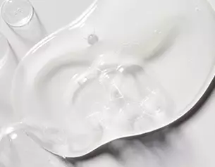 Clear, gel-like substance pooled on a smooth surface, reflecting light and creating subtle textures.
