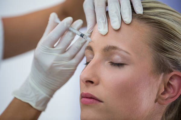 Une femme subit un traitement esthetique avec une injection dans le front.