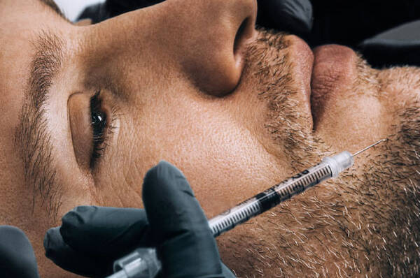 Un gros plan d'un homme avec une seringue pres de son visage, tandis qu'une infirmiere realise la procedure.