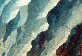 Details colores et textures d'un cristal, presentant des stries bleues, blanches et ocres sous une lumiere brillante.