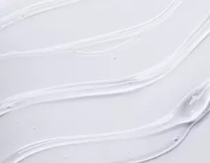 Witte, romige textuur met zachte, vloeiende lijnen op een lichte achtergrond, die doet denken aan een huidverzorgings- of cosmetisch product.