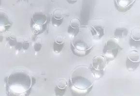 Gouttes d'eau transparentes et bulles flottant sur une surface claire, creant une texture delicate et lumineuse.