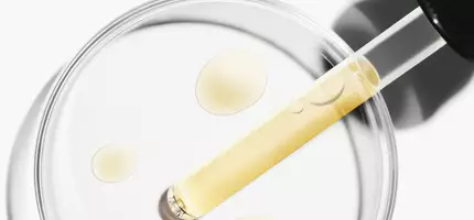 Een pipet met een gele vloeistof boven een petrischaal met druppels van dezelfde vloeistof.