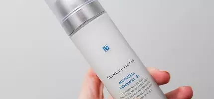 Een hand houdt een flesje van Skinceuticals Metacell Renewal B, een gezichtserum met een blauwe en zilveren dop.