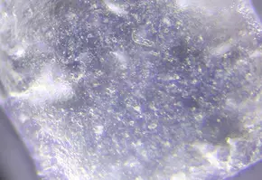 Close-up view of a translucent crystal, showcasing its surface texture and reflective properties under light.