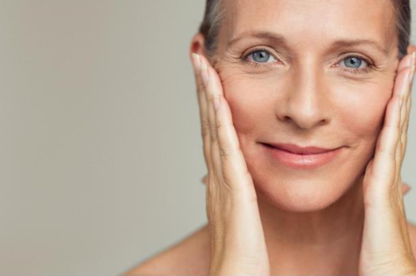 Une femme a la peau radieuse pose ses mains sur son visage et sourit.
