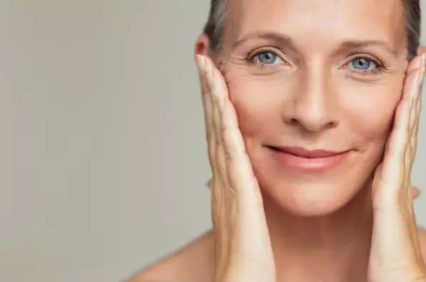 Une femme a la peau radieuse pose ses mains sur son visage et sourit.