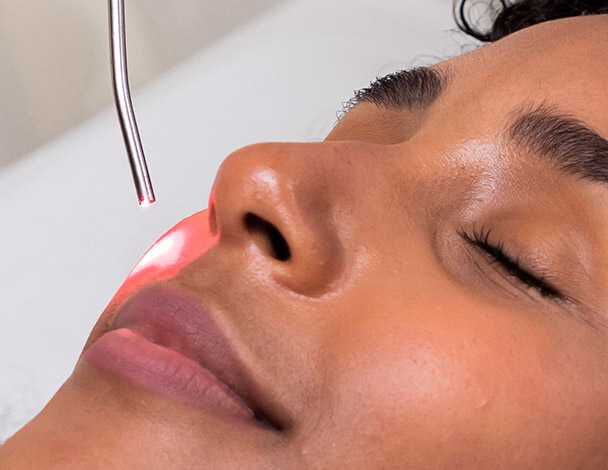 Femme aux yeux fermes subissant un traitement cutane avec un systeme laser.