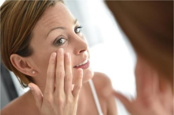 Femme aux cheveux courts regarde dans le miroir et applique une creme pour prendre soin de sa peau.