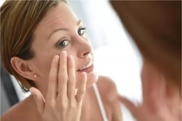 Femme aux cheveux courts regarde dans le miroir et applique une creme pour prendre soin de sa peau.