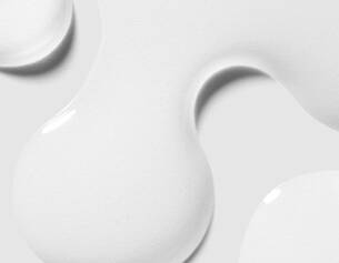 Close-up of smooth, glossy white paint droplet on a light background, highlighting its fluid shape and texture.