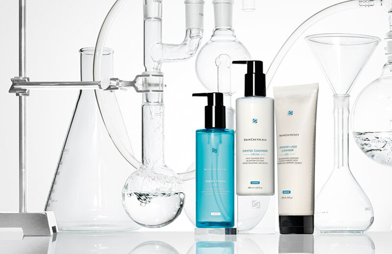 Trois flacons de nettoyants pour le visage sont places parmi de la verrerie de laboratoire contenant de l'eau et d'autres liquides.