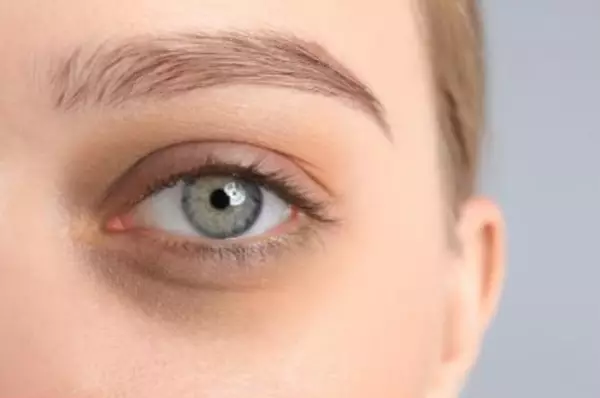 Gros plan sur l'oeil d'une femme avec une iris verte claire et un teint de peau neutre.