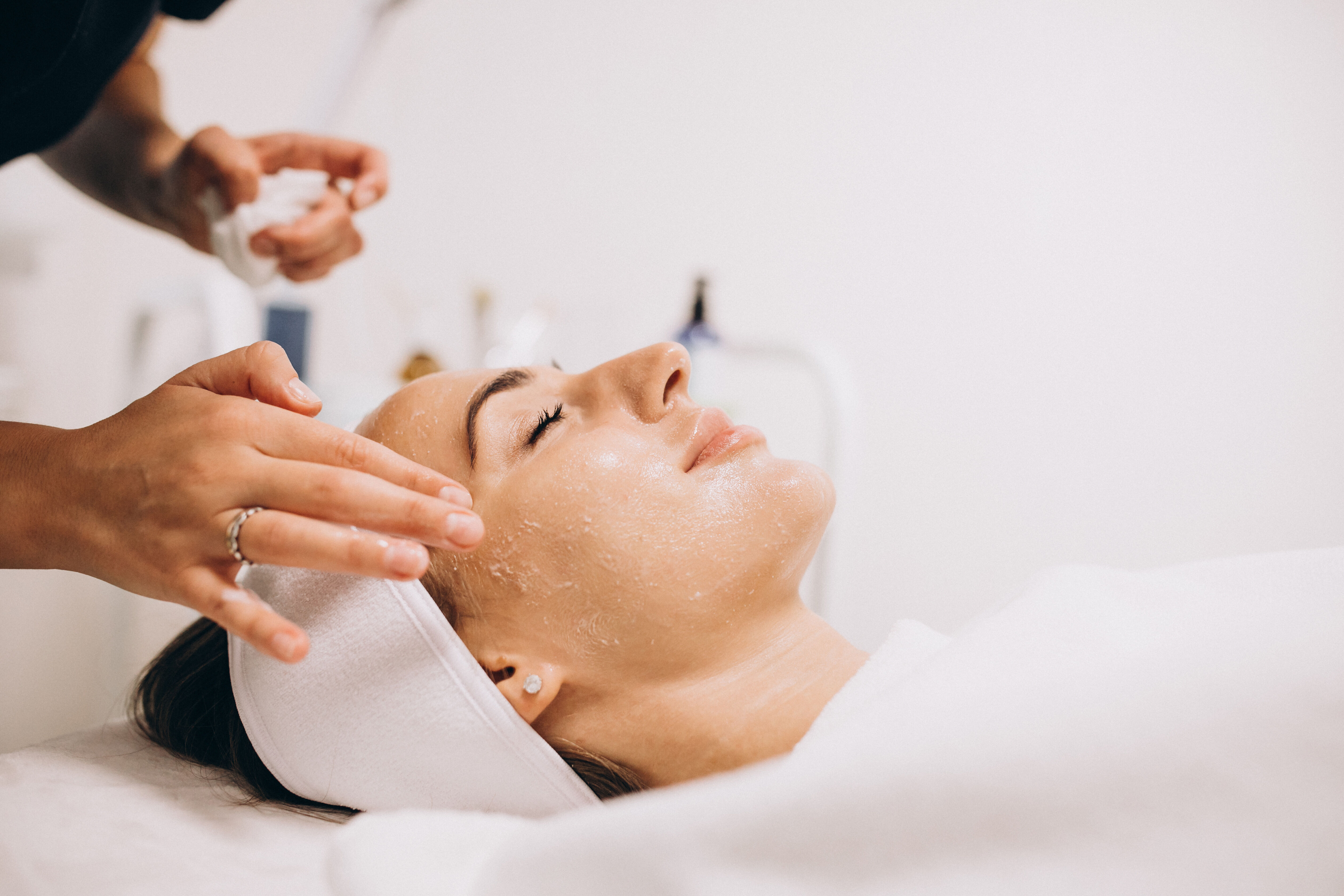 Une femme recoit un soin du visage en position allongee sur une table de traitement. Un professionnel applique des techniques manuelles sur son visage.
