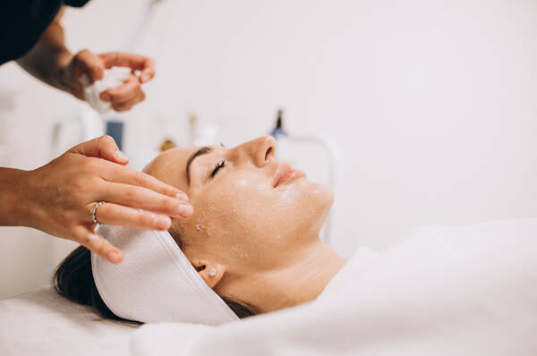 Une femme recoit un soin du visage en position allongee sur une table de traitement. Un professionnel applique des techniques manuelles sur son visage.