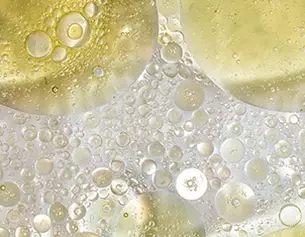 Gros plan d'une surface de bulles et de gouttelettes d'huile doree sur un fond transparent.