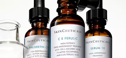 Drie flessen met huidverzorgingsserums van SkinCeuticals, waaronder C E Ferulic, Phloretin CF en Serum 10, staan op een schap met een pipet en een glazen houder.