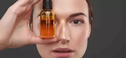 Een vrouw houdt een flesje gezichtsolie voor haar gezicht.