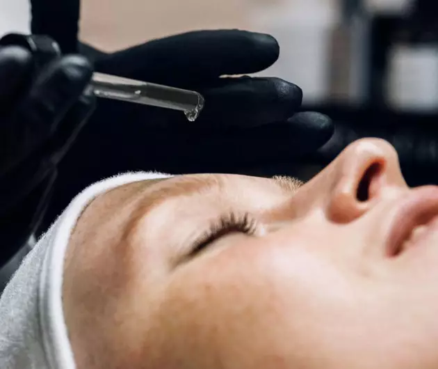 Een vrouw ondergaat een gezichtsbehandeling, terwijl een professional een serum op haar huid aanbrengt.