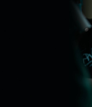 Alt-tekst: Een chirurg in een operatiekamer draagt een cap met het logo "PWRS" en een mondmasker. Hij heeft een speciaal visier met vergrotende lenzen en is geconcentreerd bezig met een medische ingreep.